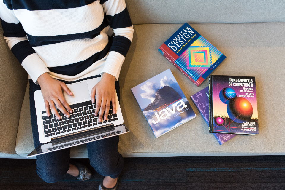 Developer using a laptop beside programming and software design books